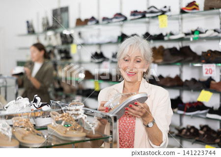 Mature woman client is demanding to inspect sandals in shoe showroom 141223744