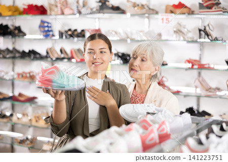 Two positive women of different ages choose new sneakers together in fashion store Two positive women of different ages choose new sneakers together in fashion store 141223751