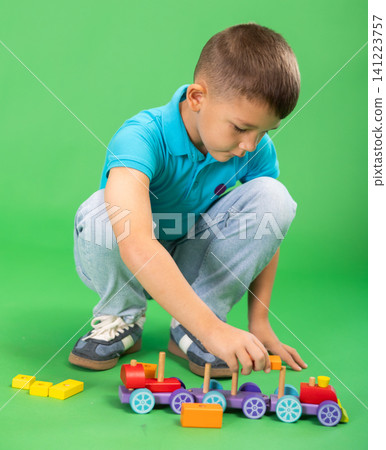 Boy in blue clothes playing with toy wooden train on green background Boy in blue clothes playing with toy wooden train on green background 141223757