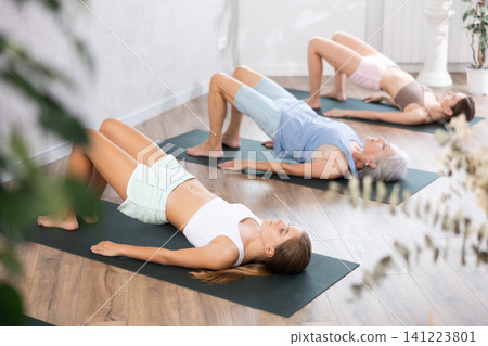 Mom, grandma and teen daughter do half bridge Setu Bandha Sarvangasana, glute bridge pose 141223801