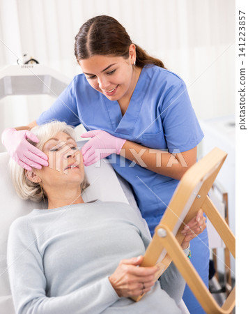 Old woman having consultation about face aesthetic while looking in the mirror Old woman having consultation about face aesthetic while looking in the mirror 141223857
