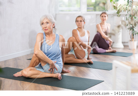 Portrait of women different ages practicing Matsyendrasana known as Lord of Fishes Pose during group yoga training in studio 141223889