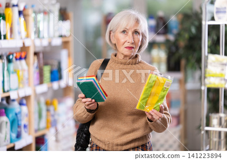 Elderly housewife chooses sponges for washing dishes and tiles in supermarket Elderly housewife chooses sponges for washing dishes and tiles in supermarket 141223894
