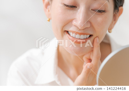 一位中年婦女面帶微笑地看著自己的嘴。 一位中年婦女面帶微笑地看著自己的嘴。 141224416