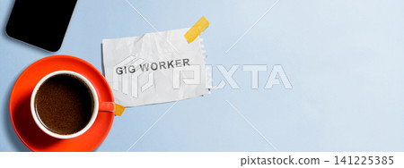 Flat lay of a cup of black coffee in an orange mug, a smartphone, and a crumpled paper note with 'Gig Worker' text taped to a light blue background. Banner with copy space Flat lay of a cup of black coffee in an orange mug, a smartphone, and a crumpled paper note with 'Gig Worker' text taped to a light blue background. Banner with copy space 141225385