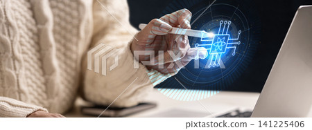 A close-up of a person wearing a knit sweater interacting with a holographic quantum processor chip interface using a digital stylus pen, representing advanced technology, AI, and computing A close-up of a person wearing a knit sweater interacting with a holographic quantum processor chip interface using a digital stylus pen, representing advanced technology, AI, and computing 141225406