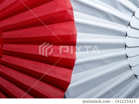 A close-up macro photograph highlighting the contrasting textures and vibrant colors of red and white fabric pleated folds on a handheld fan, creating an abstract geometric pattern A close-up macro photograph highlighting the contrasting textures and vibrant colors of red and white fabric pleated folds on a handheld fan, creating an abstract geometric pattern 141225423