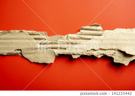Ripped and torn strip of corrugated brown cardboard showing its internal texture, set against a vibrant, bright red paper background. Great for copy space or texture Ripped and torn strip of corrugated brown cardboard showing its internal texture, set against a vibrant, bright red paper background. Great for copy space or texture 141225442