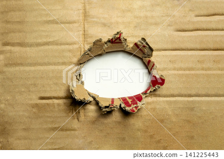 A ragged, circular hole torn through a brown corrugated cardboard sheet, revealing an empty white background. Perfect for framing messages, copy space, or design concepts A ragged, circular hole torn through a brown corrugated cardboard sheet, revealing an empty white background. Perfect for framing messages, copy space, or design concepts 141225443