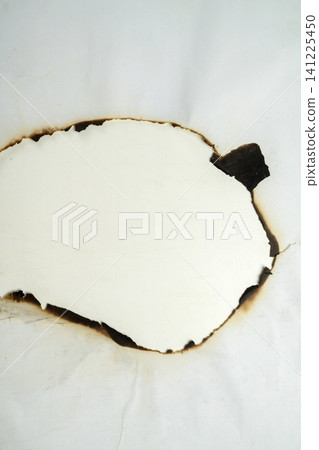 A close-up shot of a white sheet of paper with an irregular hole burned in the center, featuring charred black and brown edges A close-up shot of a white sheet of paper with an irregular hole burned in the center, featuring charred black and brown edges 141225450