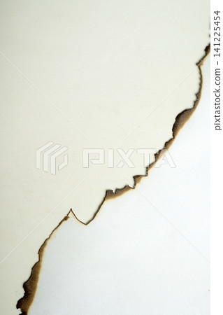 A close-up shot of a white sheet of paper with an irregular hole burned in the center, featuring charred black and brown edges A close-up shot of a white sheet of paper with an irregular hole burned in the center, featuring charred black and brown edges 141225454
