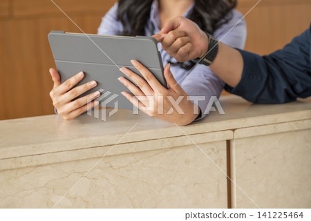 Close-up of a hotel receptionist showing digital tablet information to a guest at the front desk counter 141225464