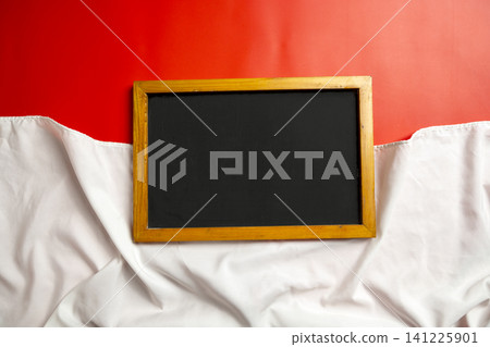 A blank rectangular chalkboard framed in wood, placed against a vibrant red background draped with textured white fabric, perfect for festive, holiday, or creative promotional messaging A blank rectangular chalkboard framed in wood, placed against a vibrant red background draped with textured white fabric, perfect for festive, holiday, or creative promotional messaging 141225901