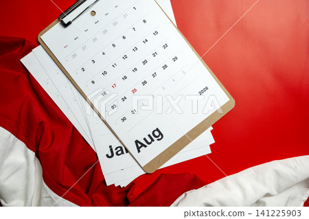 A flat-lay view of an August 2026 calendar page attached to a wooden clipboard, resting on a textured red and white fabric background, suggesting planning, schedule management, or national holidays A flat-lay view of an August 2026 calendar page attached to a wooden clipboard, resting on a textured red and white fabric background, suggesting planning, schedule management, or national holidays 141225903