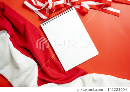 A blank white spiral notepad placed over red and white Indonesian flag fabrics, perfect for Independence Day celebration messaging, patriotic design mockups, or national events A blank white spiral notepad placed over red and white Indonesian flag fabrics, perfect for Independence Day celebration messaging, patriotic design mockups, or national events 141225904