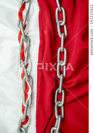 Close-up of vertical steel chains draped over textured red and white fabric, with one chain interwoven with a decorative red and white ribbon, creating a stark contrast Close-up of vertical steel chains draped over textured red and white fabric, with one chain interwoven with a decorative red and white ribbon, creating a stark contrast 141225922