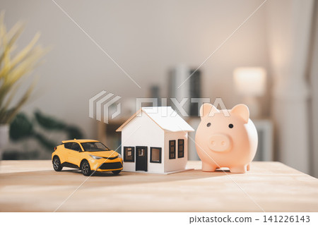 Pink piggy bank sits beside white house model and yellow car on wooden table, money saving and planning help property purchase, residential mortgage ensures real estate invest success 141226143