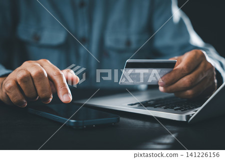 Paying, shopping, credit, card, mobile, phone, computer, home, business, concept shown by hands of man holding plastic card and touching screen of smartphone for online transaction Paying, shopping, credit, card, mobile, phone, computer, home, business, concept shown by hands of man holding plastic card and touching screen of smartphone for online transaction 141226156
