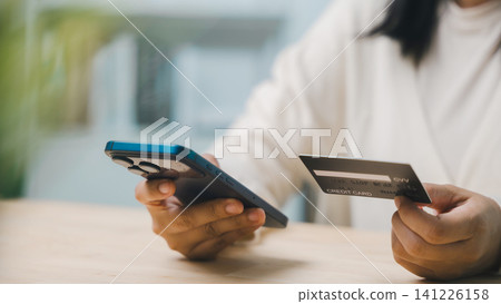 Paying and shopping with credit card, mobile phone and computer for home business concept, close up of woman hands holding smart phone and debit card for online payment Paying and shopping with credit card, mobile phone and computer for home business concept, close up of woman hands holding smart phone and debit card for online payment 141226158