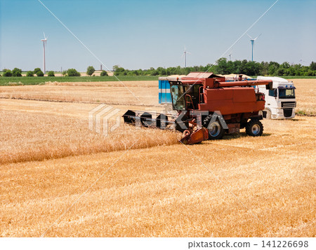 Harvest season combine harvester in golden field with sustainable energy turbines 141226698