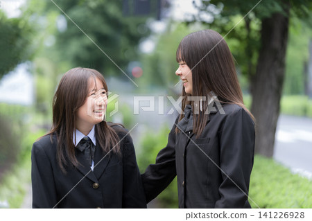 兩名日本高中女生面帶微笑,並肩而行,在戶外綠色的背景下交談,描繪了她們的高中生活和青春。 兩名日本高中女生面帶微笑,並肩而行,在戶外綠色的背景下交談,描繪了她們的高中生活和青春。 141226928