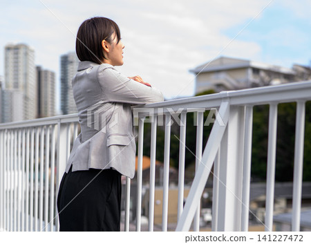 一位女商人倚靠在屋頂的欄桿上，凝視著遠方。 141227472