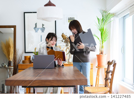 A woman operating a laptop and another woman holding documents A woman operating a laptop and another woman holding documents 141227485