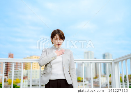 A Japanese woman in her 20s places her hand on her chest in relief on an outdoor rooftop. A Japanese woman in her 20s places her hand on her chest in relief on an outdoor rooftop. 141227513