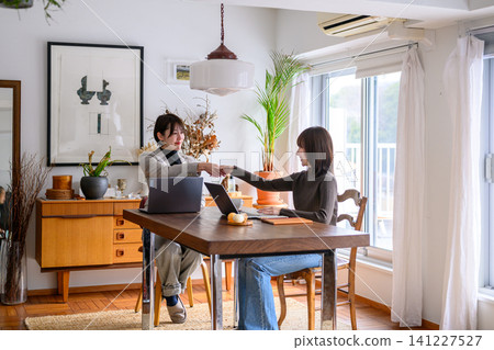 Two women shaking hands in an office with a laptop. Two women shaking hands in an office with a laptop. 141227527
