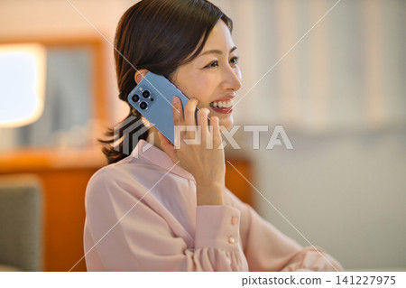 一位四十多歲的女性晚上在房間裡放鬆，看著她的智慧型手機。 141227975