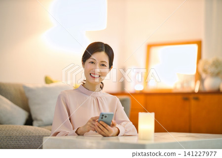 一位四十多歲的女性晚上在房間裡放鬆,看著她的智慧型手機。 一位四十多歲的女性晚上在房間裡放鬆,看著她的智慧型手機。 141227977