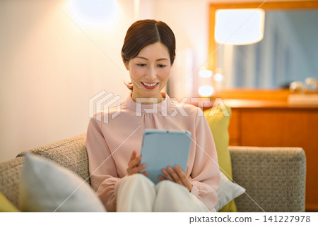 一位四十多歲的女性晚上在房間裡放鬆地看著平板電腦。 一位四十多歲的女性晚上在房間裡放鬆地看著平板電腦。 141227978