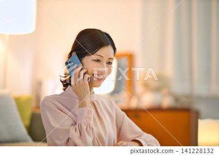 一位四十多歲的女性晚上在房間裡放鬆,看著她的智慧型手機。 一位四十多歲的女性晚上在房間裡放鬆,看著她的智慧型手機。 141228132