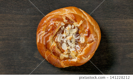 Freshly Baked Sweet Bun with Caramel Filling and Almond Flakes on Dark Wooden Table, Top View 141228212
