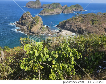 A breathtaking high-angle ocean view from a wooden viewpoint structure, showcasing lush green rocky islets scattered across the vibrant blue sea under the clear sky on a sunny summer day in Indonesia. 141228350