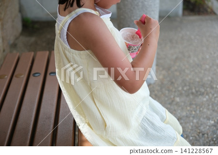 A child eating ice cream on a bench in the shade of a park. A child eating ice cream on a bench in the shade of a park. 141228567