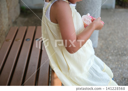A child eating ice cream on a park bench in the summer. A child eating ice cream on a park bench in the summer. 141228568