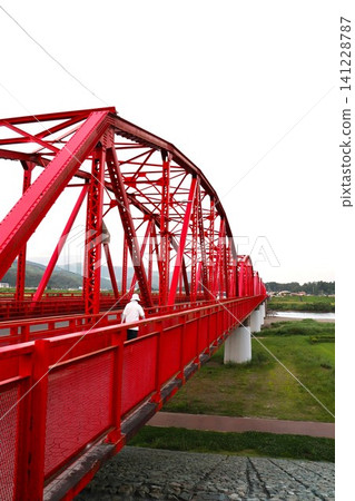 The back view of a person walking on the pedestrian walkway of a red iron bridge. The back view of a person walking on the pedestrian walkway of a red iron bridge. 141228787