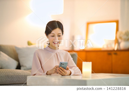 A woman in her 40s relaxing in her room at night and looking at her smartphone. A woman in her 40s relaxing in her room at night and looking at her smartphone. 141228816