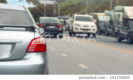 Rear view shot of a silver car on a road. With other vehicles driving ahead. The setting is a busy highway during the daytime. Showing light traffic flow under a clear sky. Traffic in Rayong Thailand. Rear view shot of a silver car on a road. With other vehicles driving ahead. The setting is a busy highway during the daytime. Showing light traffic flow under a clear sky. Traffic in Rayong Thailand. 141230005
