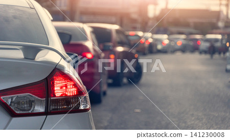 Rear view shot of a silver car waiting in heavy city traffic during the day. The bright red tail light is highlighted as multiple vehicles queue up on the road creating a busy commute scene. Rear view shot of a silver car waiting in heavy city traffic during the day. The bright red tail light is highlighted as multiple vehicles queue up on the road creating a busy commute scene. 141230008