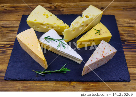Set of various types of cheese on black slate board on a wooden table Set of various types of cheese on black slate board on a wooden table 141230269