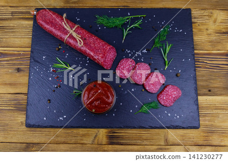 Salami sausage with ketchup and spices on black slate board on a wooden table 141230277