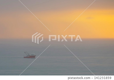 Red fishing boat sailing in misty sea at golden sunset with copy space 141231859