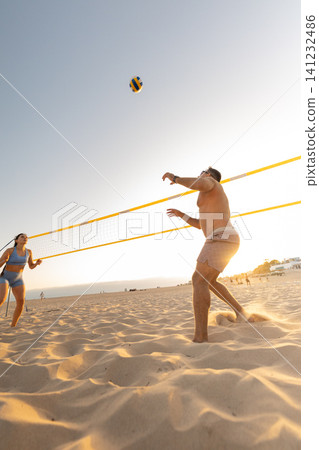 People playing beach volleyball on sand at sunset People playing beach volleyball on sand at sunset 141232486