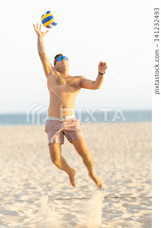 Male athlete jumping, spiking volleyball on beach 141232493
