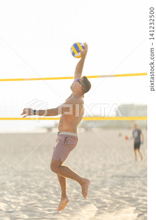 Male athlete spiking volleyball during beach game Male athlete spiking volleyball during beach game 141232500