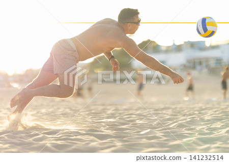 Man diving for volleyball on sandy beach at sunset 141232514