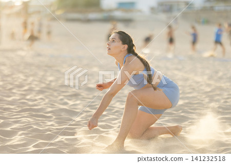 Female athlete playing beach volleyball on sand at sunset Female athlete playing beach volleyball on sand at sunset 141232518