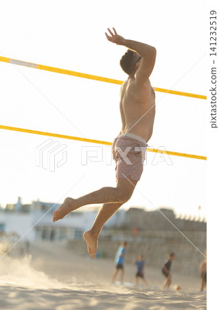Man jumping over net playing beach volleyball 141232519